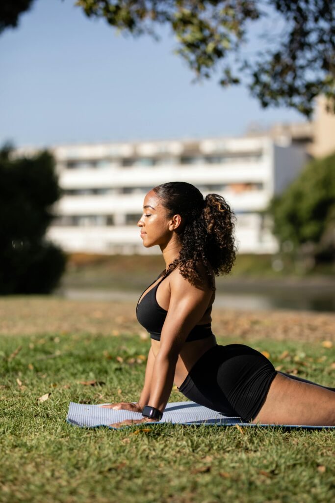 Side view of a woman performing yoga on a mat in a sunny, outdoor park.