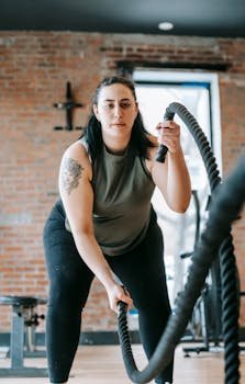 Low angle of concentrated female in sportswear exercising with heavy battle ropes during intense functional training